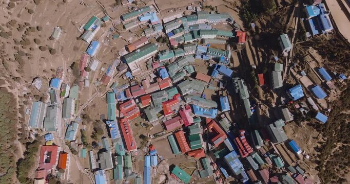 Aerial top-down view of Namche Bazaar, then pulling out to reveal the nestled amphitheater village surrounded by dense forest and snow-capped Himalayan peaks in Nepal.