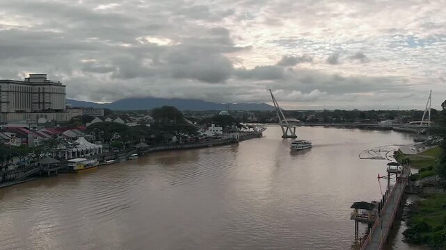 Aerial view of Kuching waterfront promenade with Darul Hana Bridge and boats on the Sarawak River under cloudy skies