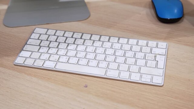 Close-up view of a wireless bilingual computer keyboard on a wooden desk beside a mouse in an indoor office workspace, highlighting modern desktop technology and everyday typing setup.