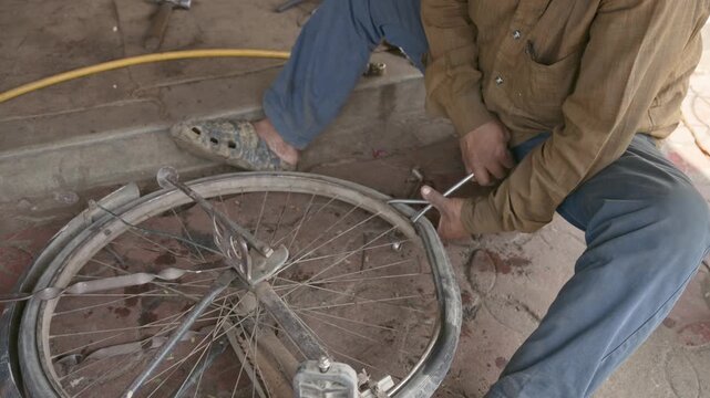 Close up of a local Indian mechanic using metal tools to fix a flat tire and spokes on a bicycle wheel. Authentic street scene showing manual labor and repair work.