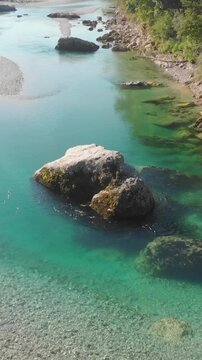drone flying above emerald Soca river with giant rock on early summer morning, vertical shot