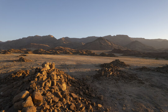 Aerial view of a landscape bathed in the warm glow of the setting sun, where rocky outcrops punctuate the ochre earth leading to distant mountains, Windhoek, Namibia.