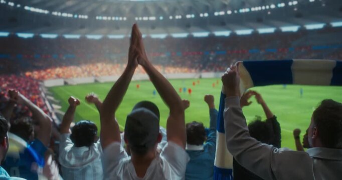 Back view Soccer Supporters Celebrate in a Packed Stadium, Raising hands andDuring a Professional Worl Championship Match, as the Crowd Roars Around the Field. Big Euro Event