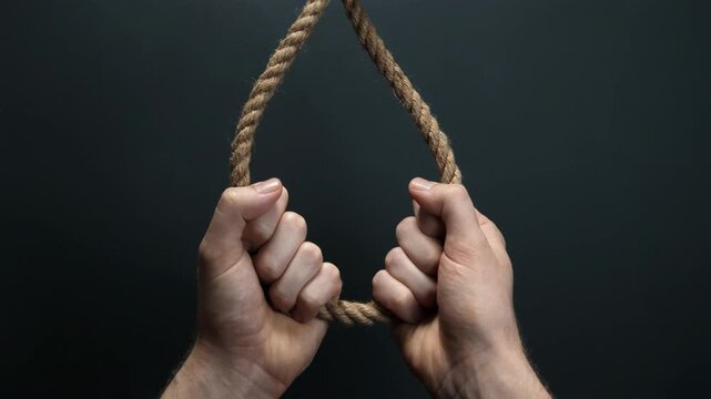 Human hands pulling and tightening a thick rope with a hangman's knot against a dark background