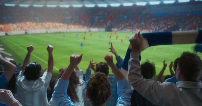 Back view of Fans Cheer for Their Team on a Stadium During Soccer Championship Match. Teams Play, Crowds of Fans Celebrate Victory, Goal. Football Cup Tournament. Medium Shot