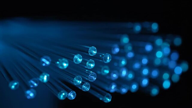Close-up of glowing blue fiber optic strands transmitting light data on a dark background