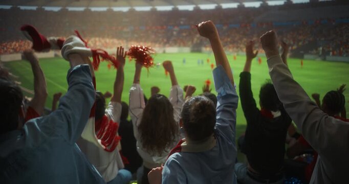 Rear View of Diverse Soccer Supporters in a Packed Stadium, Clapping, Raising hands and Waving Red White Scarves in Slow Motion During an International Championship Match Field