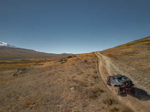 Aerial view of a powerful off-road buggy UTV driving fast on a dusty mountain dirt road during a desert expedition, speed and extreme sports adventure travel concept.