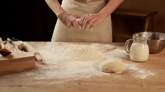 Baker breaking an egg into flour on a wooden table while making dough for homemade bread, cake or pasta in slow motion