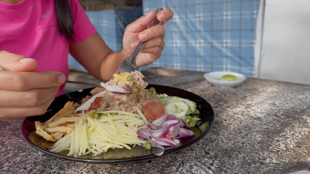 Woman eating thai fried rice street food outdoors, asian cuisine in side view with copy space and fresh vegetables on plate.