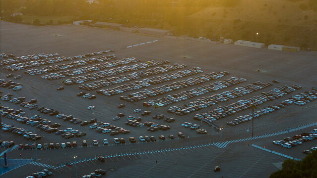 Aerial view of rows of cars filling the vast parking lot near 1000 Vin Scully Ave under a soft, golden sunset, Los Angeles, California, United States.
