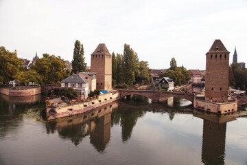 Obraz premium Historic building with tower and bridge reflecting in water, surrounded by trees in old town Strasbourg, France, showcasing traditional architecture