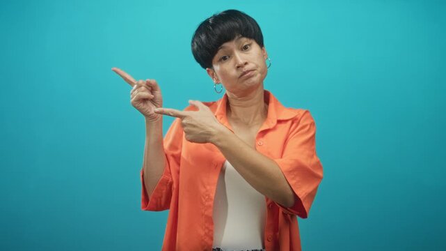 Woman pointing index fingers with dismissive face and visible fingers, wearing orange shirt in studio; skepticism casual attitude.