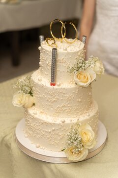 Elegant wedding cake with rings and white flowers, held by newlyweds in celebration