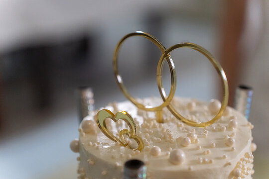 Elegant wedding cake with rings and white flowers, held by newlyweds in celebration