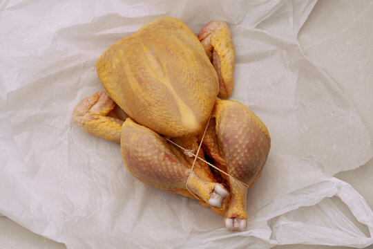 Still life of raw boiler chicken tied with twine on white parchment paper
