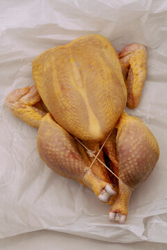 Close up view from above of tied, seasoned raw chicken on white parchment paper
