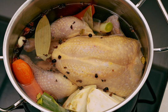View from above of a whole raw chicken in a pot with chicken stock and vegetables
