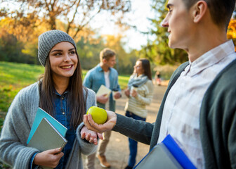 Student giving apple to friend in autumn park.