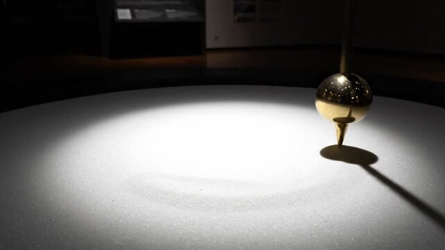 Brass Foucault Pendulum Sphere Demonstrating Earth Rotation on a White Surface with Spotlight