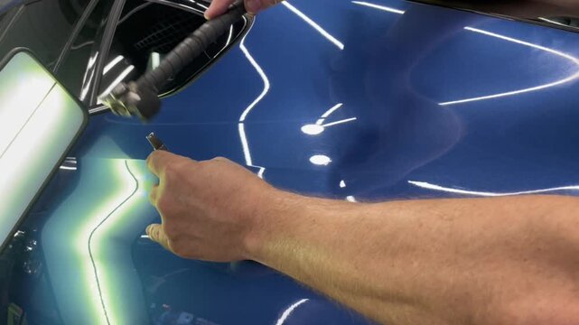 PDR. Process of paintless dent repair on car body. The mechanic at the auto shop with tools to repair dents in car body. Body repair. A specialist repairs a dent on the car body without painting.