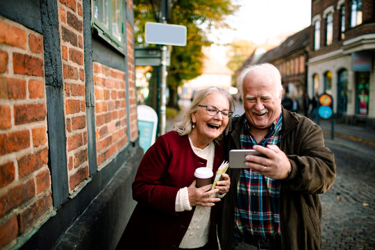 Smiling senior couple taking smartphone selfie on historic city street