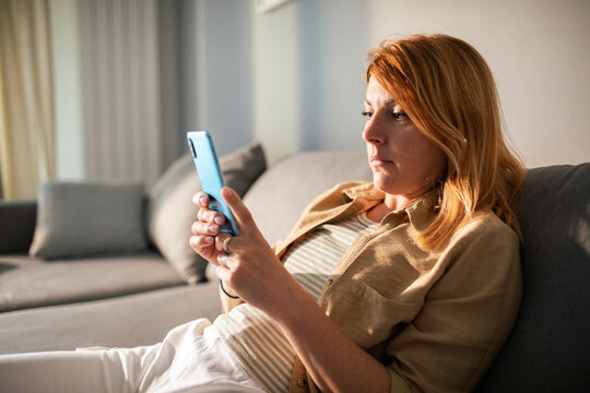 Woman using smartphone on living room sofa at home