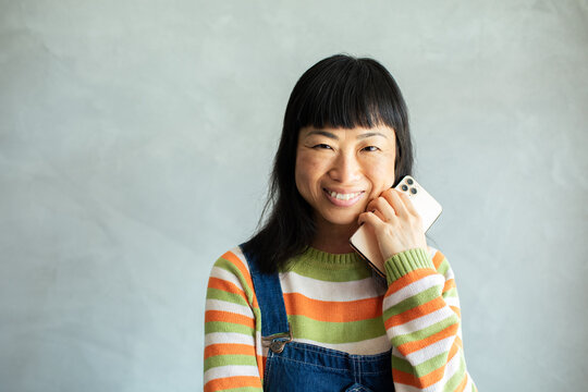 Smiling woman holding smartphone against gray wall