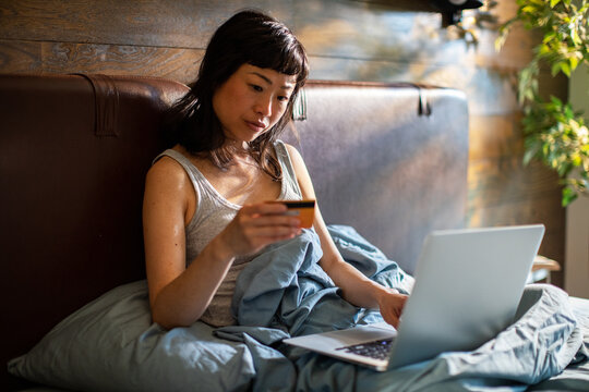 Young woman shopping online with credit card in bed at home