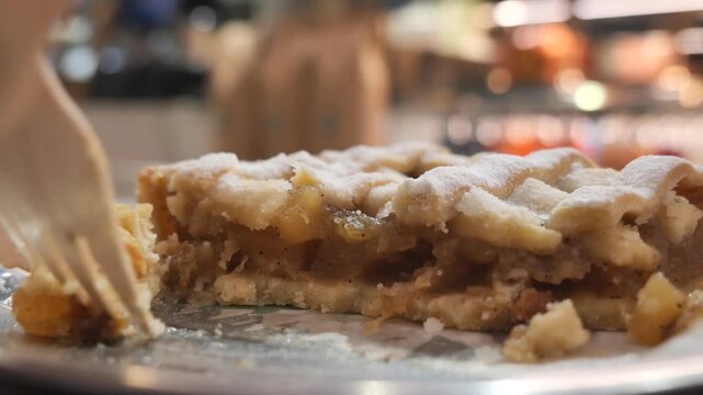 Close up of fork cutting apple pie slice on plate with powdered sugar topping.