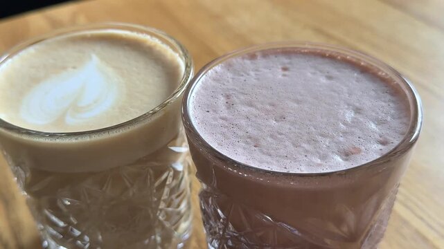 Two hot drinks placed together, cappuccino with milk foam and heart art next to glass of cocoa, taste comparison, choice concept, cafe menu options, cozy atmosphere.