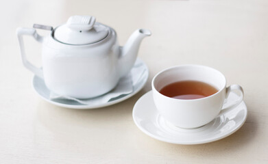 Fototapeta premium A white teapot and a cup of hot tea on a light surface