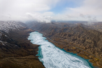 An aerial view shows a partially frozen lake winding through the dramatic, rugged landscape of the Qilian Mountains in China © AS_SleepingPanda