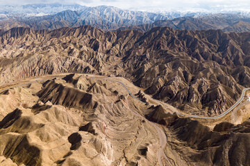 Naklejka premium Vast danxia landform formations in the Qilian Mountains of China showcase rugged, layered terrain with a winding road cutting through the arid landscape