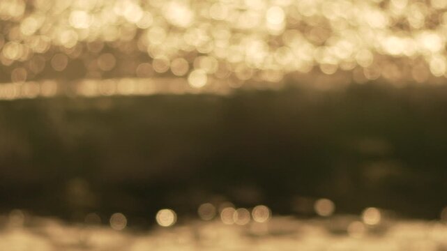 Golden bokeh water reflections shimmering during sunset or sunrise on a wavy surface to create a relaxing abstract background