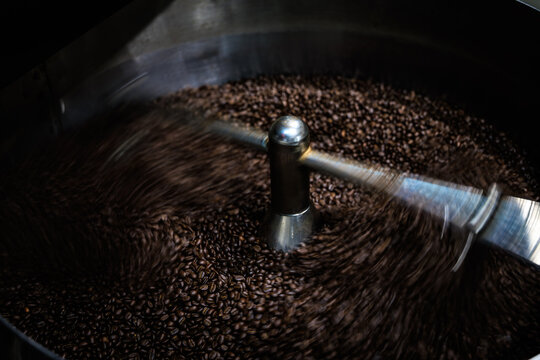 Industrial Metal Agitator Arm Mixes Fresh Dark Roasted Coffee Beans In A Cooling Tray During A Professional Cafe Manufacturing Process