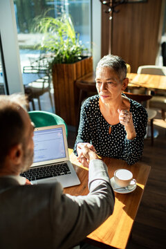 Advisor and mature woman shaking hands during consultation in cafe