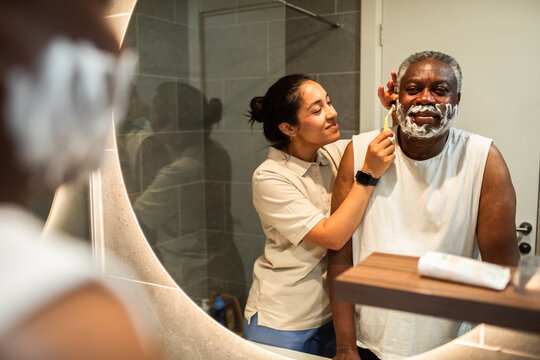 Caregiver helping senior man shave in home bathroom