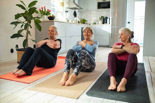 Three senior women doing core exercises in home kitchen