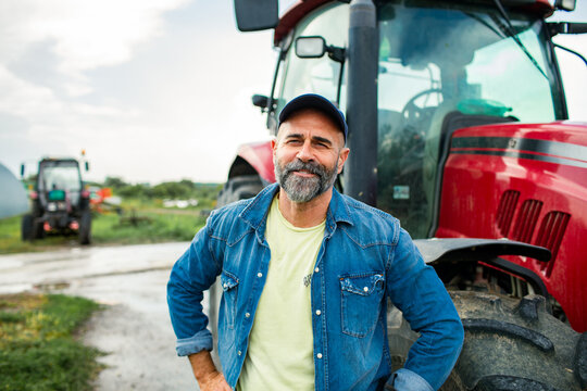 Smiling farmer standing by red tractor on farm