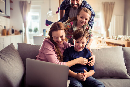 Smiling family using laptop on living room sofa