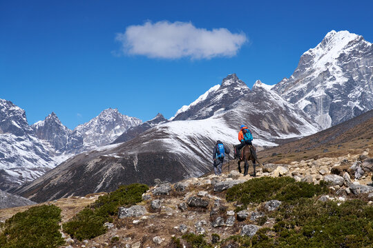 Breathtaking view of snow-capped Himalayan range under a bright sunny sky, with two trekkers on Everest Base Camp trail 