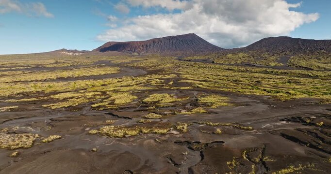 Ambrym Island volcanic landscape covered with rugged lava plains and vegetation growing around the Benbow and Marum volcanoes under a blue sky with clouds. Travel to Vanuatu. Aerial view drone flight