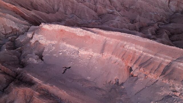 Forward flight over sculpted pink and orange Moon Valley ridges revealing San Pedro de Atacama town nestled in the vast desert plain beyond. San Pedro de Atacama, Chile