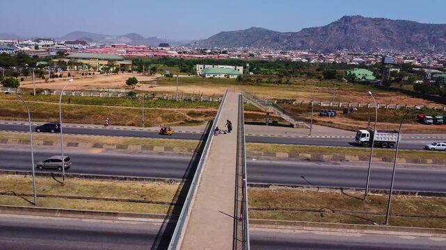 High angle view of a pedestrian overpass crossing a busy highway in Abuja, Nigeria. A local vendor sells goods on the bridge while a man is talking to him.