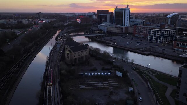 Aerial video of Trams passing  Pomona Metrolink station and the Manchester Ship Canal during a vibrant sunset in Greater Manchester, UK