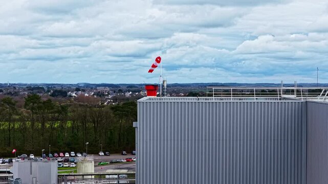 Aerial view of a factory roof with a red and white striped windsock indicates the wind direction.