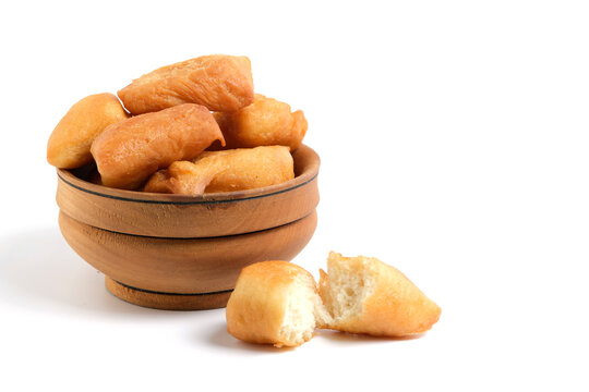 Traditional wooden bowl filled with golden brown fried dough balls, baursaks on clean white background, with one piece broken open in foreground.
