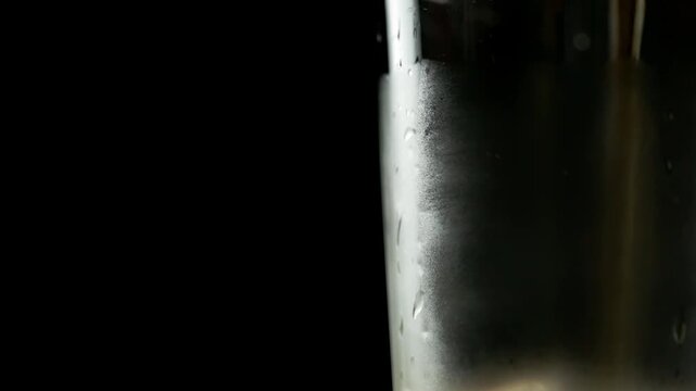 Macro view of soda being poured into a glass and ice cubes added, black background with space for text