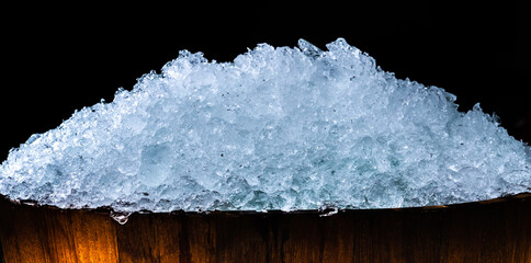 Pile of crushed ice cubes in wood bucket on dark background with copy space. Crushed ice cubes foreground for beverages, beer, whisky, fruit juice, milk, fresh food or fresh vegetables. © Fahroni